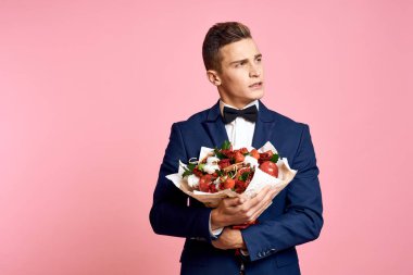 Pembe arka planda bir buket çiçekli klasik takım elbiseli yakışıklı bir adam. Papyon modeli.