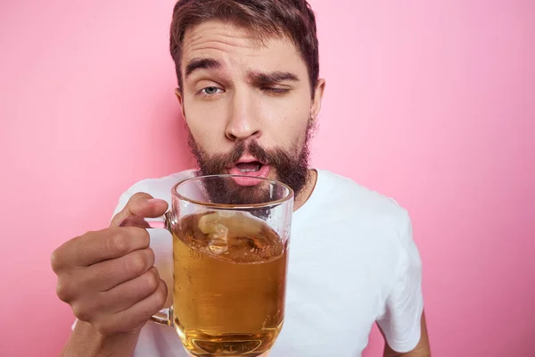 Homem bêbado com uma grande caneca de cerveja Em um fundo rosa e uma camiseta branca vista relaxada de uma barba grossa — Fotografia de Stock