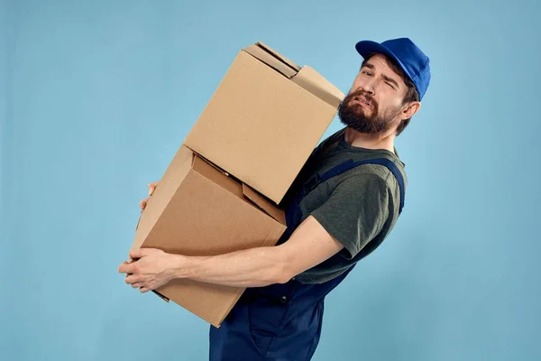 Homem em uniforme de trabalho com caixas em mãos serviço de entrega fundo azul — Fotografia de Stock
