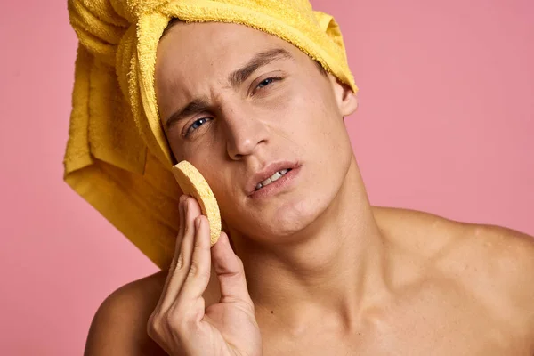 Mann mit Handtuch auf dem Kopf und gelbem Schwamm in der Hand bei kosmetischen Eingriffen die Gesichtshaut reinigen — Stockfoto