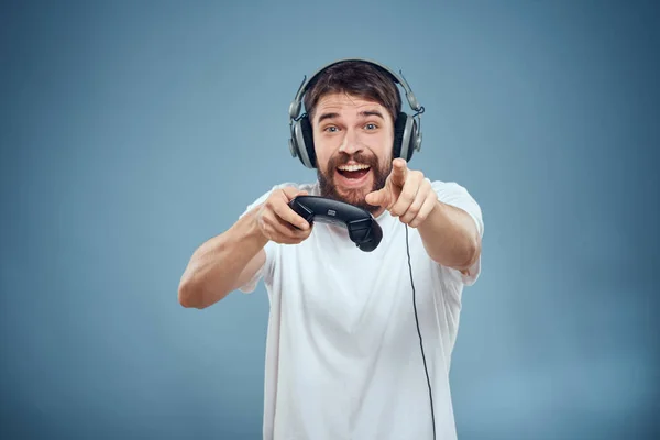 Άνδρας με ακουστικά χειριστήριο στα χέρια παίζοντας παιχνίδι κονσόλα lifestyle συναισθήματα μπλε φόντο λευκό t-shirt — Φωτογραφία Αρχείου