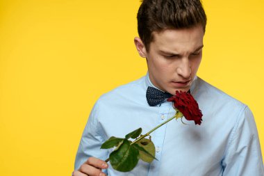 Sarı arka planda elinde kırmızı bir gül olan takım elbiseli şık bir adam.