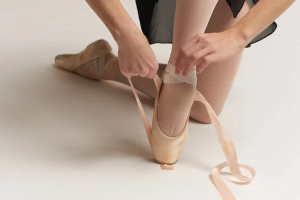 Ballerina mette scarpe da punta sui suoi piedi bianco nastro modello danza luce sfondo. — Foto Stock