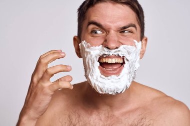 Yüzünde beyaz tıraş köpüğü olan yakışıklı bir adam ve jilet gibi omuzları olan temiz bir cilt.