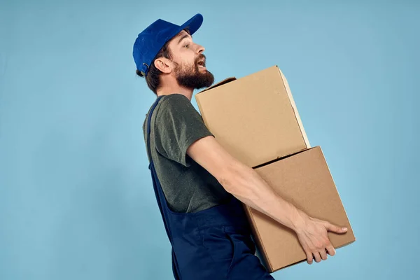 Άνδρας με στολή εργασίας με κουτιά στο χέρι υπηρεσία παράδοσης μπλε φόντο — Φωτογραφία Αρχείου