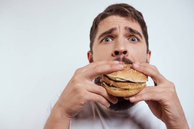Beyaz bir tişörtle arka planda hamburger yiyen bir adam yakın çekim açlık ve fast food manzarası izledi.