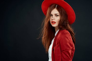 Kırmızı dudaklı güzel bir kadın ceketinde şapkası olan zarif stil cazibesi koyu tenli arka planda.