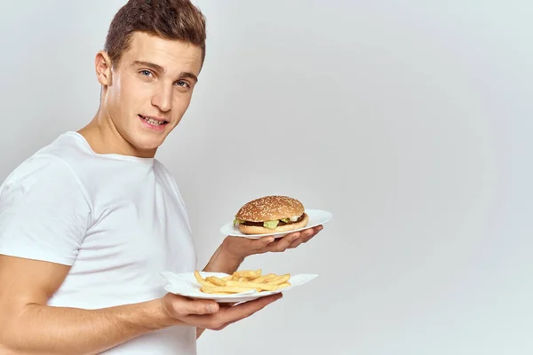 Muž s hranolky a hamburger na světlém pozadí v bílém tričku zblízka oříznutý pohled kopírovat Space Model — Stock fotografie