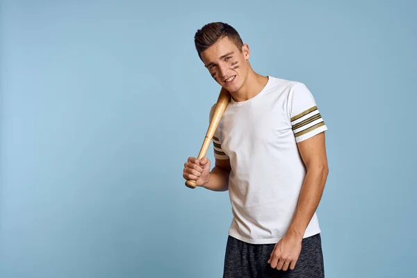 Baseballový chlap s pálkou v ruce na modrém pozadí a bojové barvy na tváři make-up model t-shirt — Stock fotografie