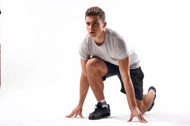 Hafif bir geçmişi olan atletik bir adam tam boy ve koşu şortu spor ayakkabısı tişörtü giyiyor.