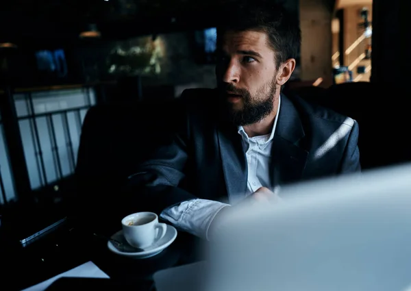 Homme d'affaires en costume dans un café devant un ordinateur portable avec une tasse de boisson officielle — Photo