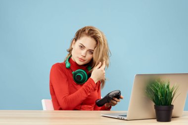 Dizüstü bilgisayar kulaklığının önündeki masada oturan bir kadın çevrimiçi yaşam tarzı mavi arka planda oynuyor.