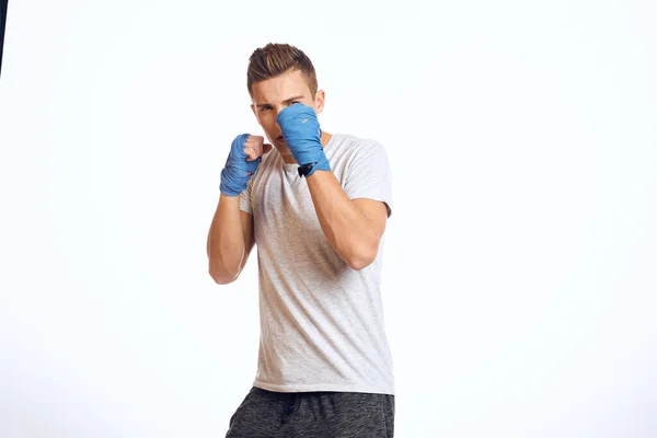 Sportovní mužský boxer v modrých rukavicích cvičení údery na světlém pozadí oříznutý pohled — Stock fotografie