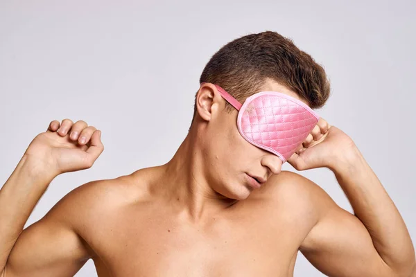 Un uomo in maschera rosa per dormire su uno sfondo chiaro di notte gesti con le mani — Foto Stock