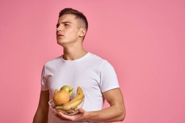 Elinde meyveler olan bir adam pembe arka planda sağlıklı yiyecek vitaminleri pembe arka planda beyaz tişört modeli
