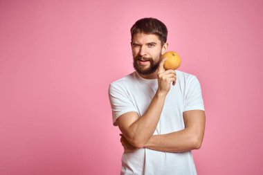 Pembe arka planda, beyaz tişörtlü, turuncu elbiseli genç bir adam. Model ellerle el kol hareketi yapmak eğlenceli.
