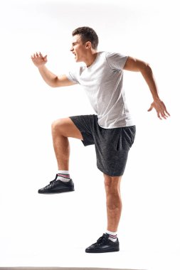 Hafif bir geçmişi olan atletik bir adam tam boy ve koşu şortu spor ayakkabısı tişörtü giyiyor.