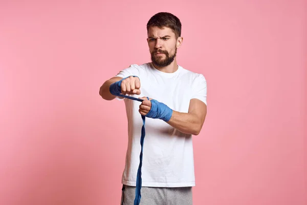 Uomo sportivo in una t-shirt bianca bendaggi boxe sulle mani di uno stile di vita di allenamento sfondo rosa — Foto Stock