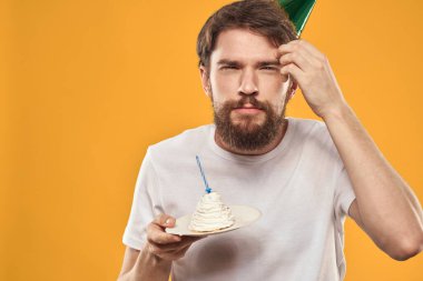 Sakallı ve şapkalı yakışıklı bir adam doğum günü partisi sarı arka planını kutluyor.
