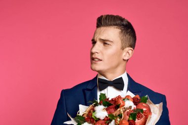 Çiçek buketi ve pembe arka planda papyonlu romantik bir adam.