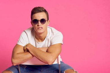 Beyaz tişörtlü ve kot pantolonlu bir adam, modern tarz pembe izole edilmiş arka planda oturuyor.