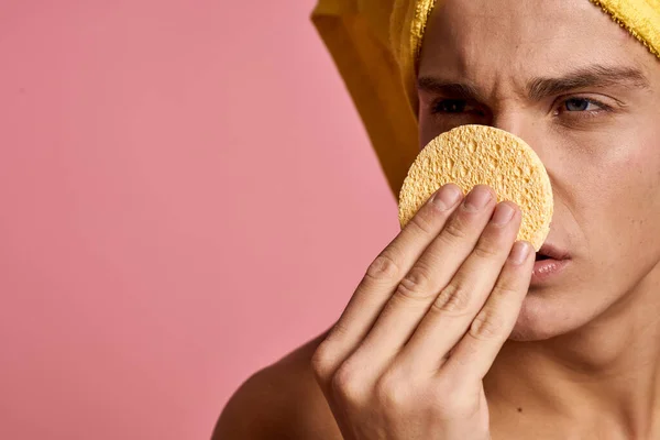 man with a towel on his head and a yellow sponge in his hand cosmetic procedure clean skin of the face