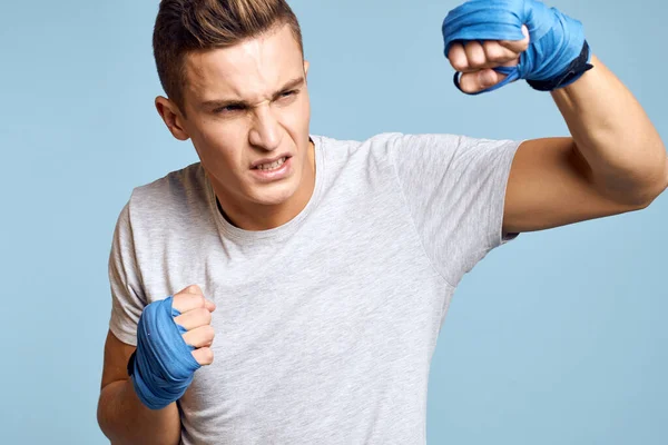 Hombre deportivo en guantes de boxeo azul y camiseta sobre fondo azul practicando golpes vista recortada — Foto de Stock