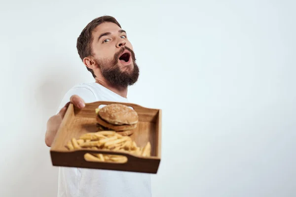 Homem com bandeja de madeira batatas fritas e hambúrguer fast food calorias modelo t-shirt branca — Fotografia de Stock