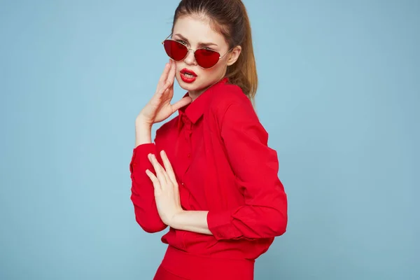 Kobieta w czerwonej koszuli na niebieskim tle trzyma ręce w pobliżu twarzy i okulary przeciwsłoneczne czerwony makijaż usta model — Zdjęcie stockowe