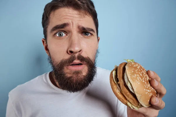 Uomo emotivo hamburger fast food dieta cibo primo piano sfondo blu — Foto Stock