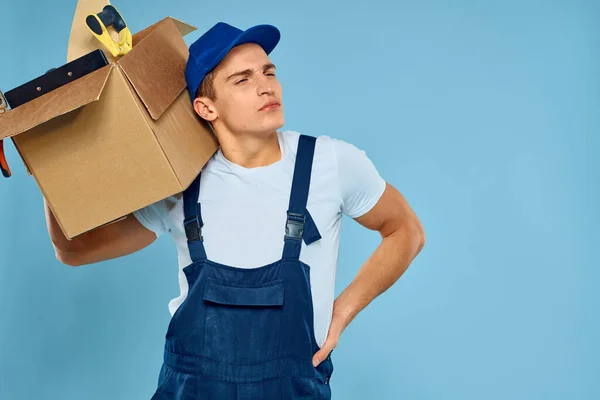 Trabalhador homem em caixa uniforme com ferramentas carregador entrega azul fundo — Fotografia de Stock