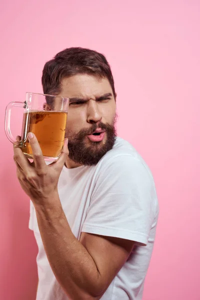 Pembe arka planda bira kupasıyla sakallı bir adam. Eğlenceli duygular beyaz tişörtlü sarhoş bir adamın görüntüsünü engelledi. — Stok fotoğraf
