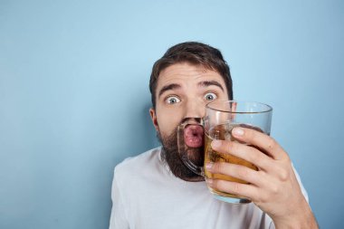 Beyaz tişörtlü, bira kupalı, sarhoş, mavi arka planlı neşeli bir adam.