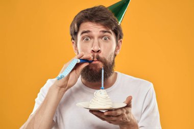Sakallı ve şapkalı yakışıklı bir adam doğum günü partisi sarı arka planını kutluyor.