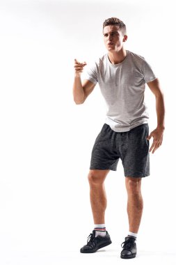 Hafif bir geçmişi olan atletik bir adam tam boy ve koşu şortu spor ayakkabısı tişörtü giyiyor.