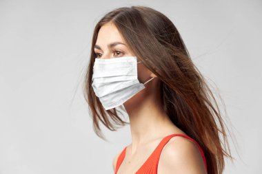 Yüzünde tıbbi bir maske var. Yan tarafa bakıyor. 