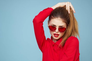 Koyu renk gözlüklü, kırmızı dudaklı, cazibeli stüdyo mavi arka planlı bir kadın.