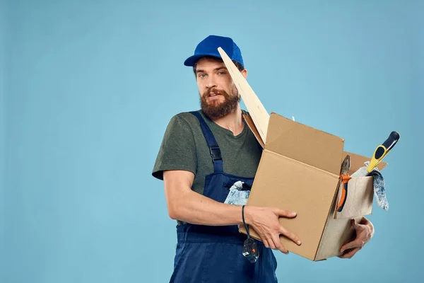 유니폼 상자 도구를 가지고 파란색 배경을 만들고 있는 노동자 — 스톡 사진