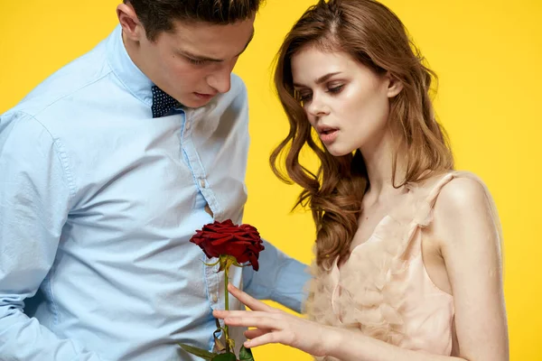 Un homme romantique étreint une femme dans une robe rouge avec une rose à la main sur un fond jaune — Photo