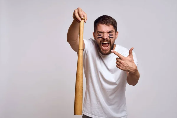 Un hombre emocional con un bate de béisbol sobre un fondo claro en una camiseta blanca está haciendo gestos con sus manos a la modelo — Foto de Stock