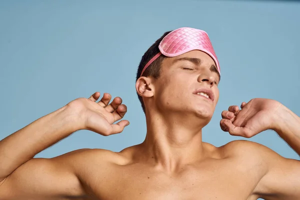 Avslappet mann med rosa sovemaske på blå bakgrunn. – stockfoto