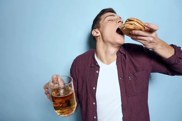 손에 야채 음식을 먹고 맥주 머그와 햄버거를 먹는 밝은 술취한 남자 — 스톡 사진