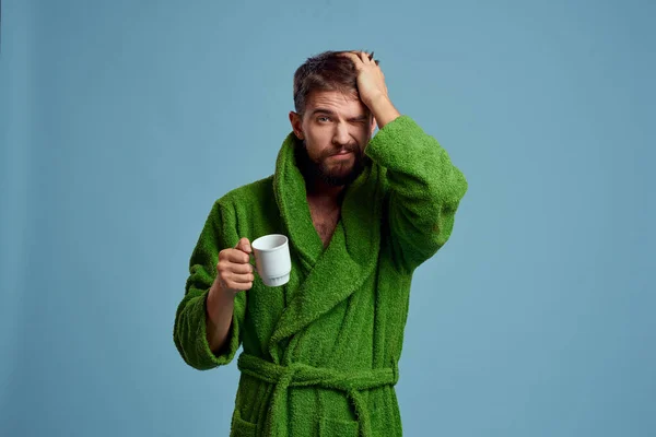 Homem congelado em um manto quente com uma xícara de bebida quente em um fundo azul vista cortada — Fotografia de Stock