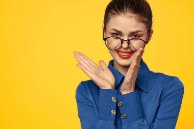 Mavi gömlekli, gözlüklü, yüzünde parlak makyajlı bir kadın elleriyle işaret ediyor.