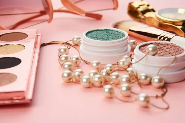 Göz falı aksesuarlar, boncuklar makyaj fırçaları pembe arka planda profesyonel kozmetik ürünleri koleksiyonu.