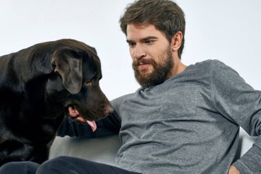 Erkek sahibi kanepede köpekle oynuyor. Eğlenceli ışık odası arkadaşları evcil hayvanı eğitiyor.
