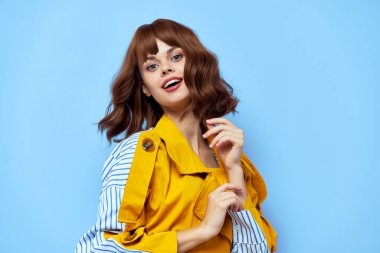 Kısa saçlı, sarı ceketli, yuvarlak düğmeli, gülümseyen kırmızı dudaklı bir kadın.