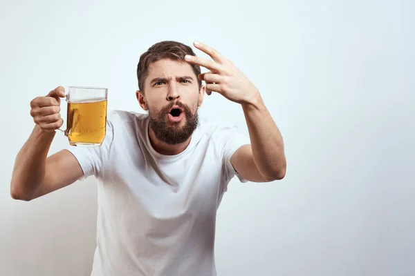 Homme avec une tasse de bière dans ses mains et un t-shirt blanc fond clair moustache barbe émotions modèle — Photo