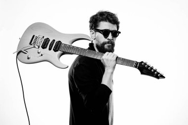 Elinde bir gitar tutan bir adam. Siyah deri ceket. Siyah gözlükler.