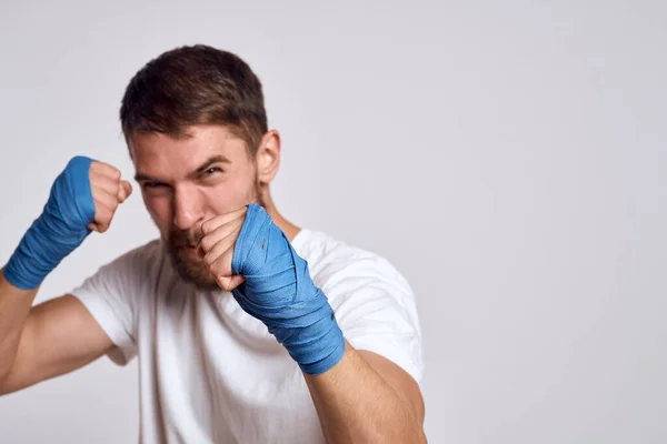 Un hombre deportivo con una camiseta blanca vendajes de boxeo en sus manos la práctica de ejercicios de golpe mejorar las habilidades — Foto de Stock